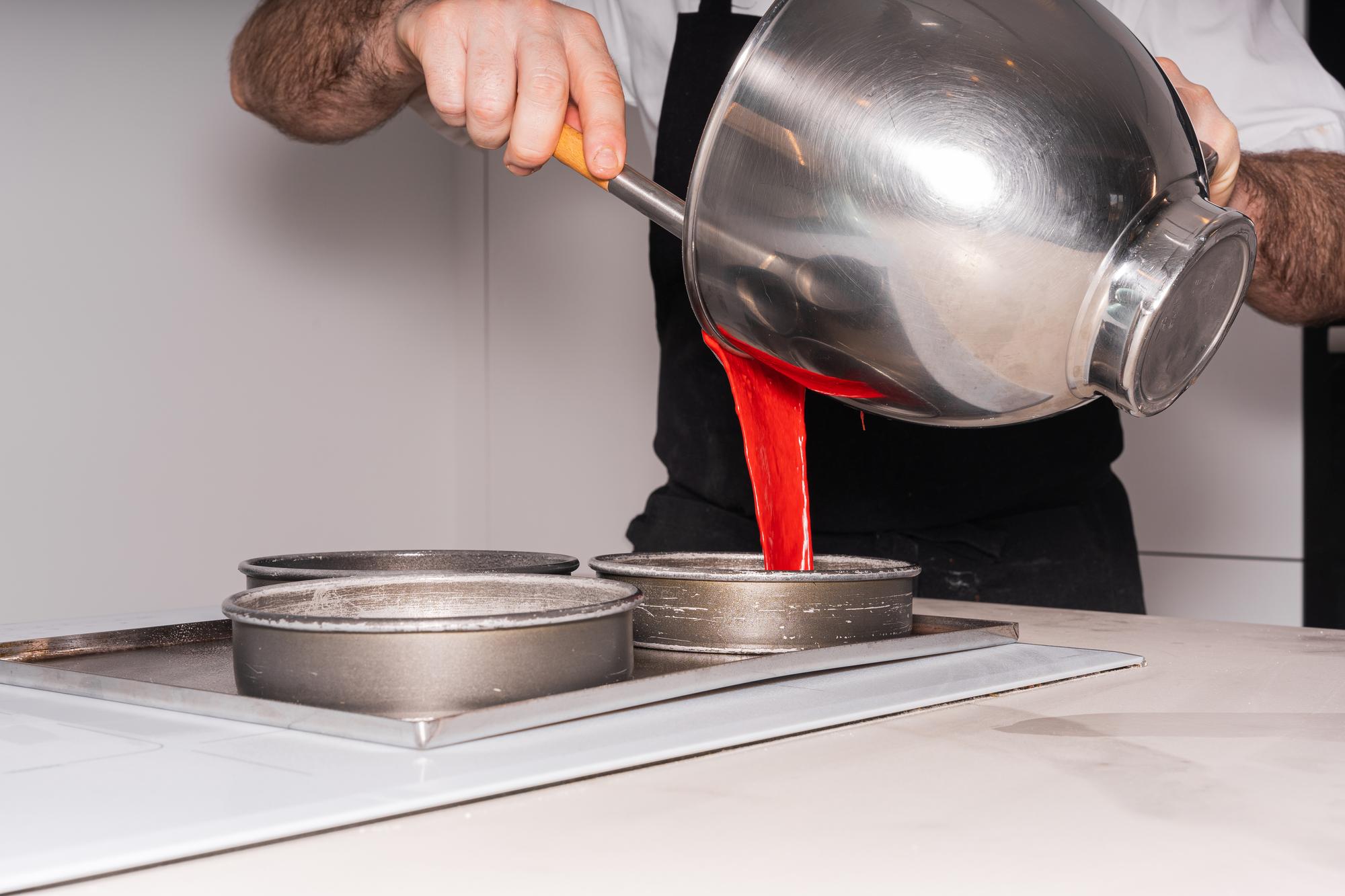 Chef at stove stirring a sauce in a stainless pan